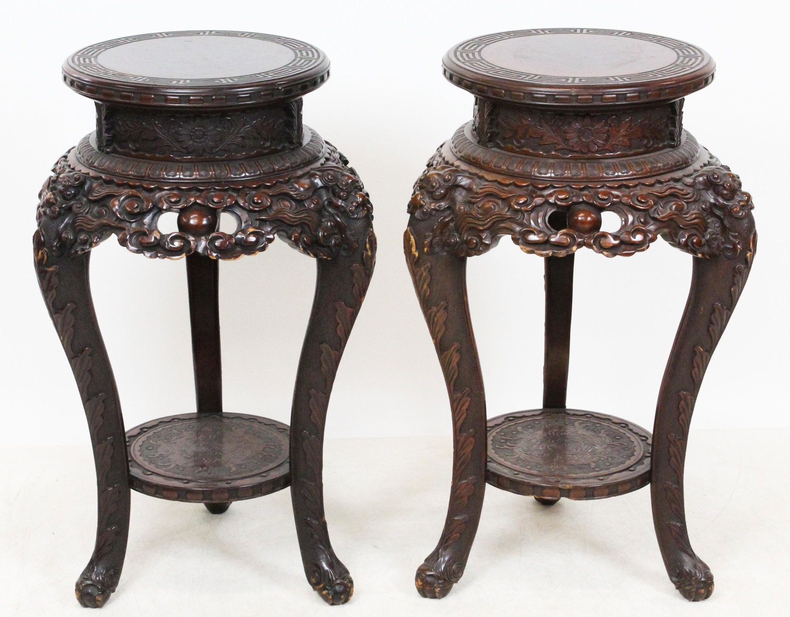 Pair Chinese Carved Stands: Ca. 1900 pair of Chinese ornate carved lamp tables, or fern stands. Round tops with key design, ornate open work carved under tops with dragon faces over 3 cabriole legs and lower shelf. 32" H, 14" Di