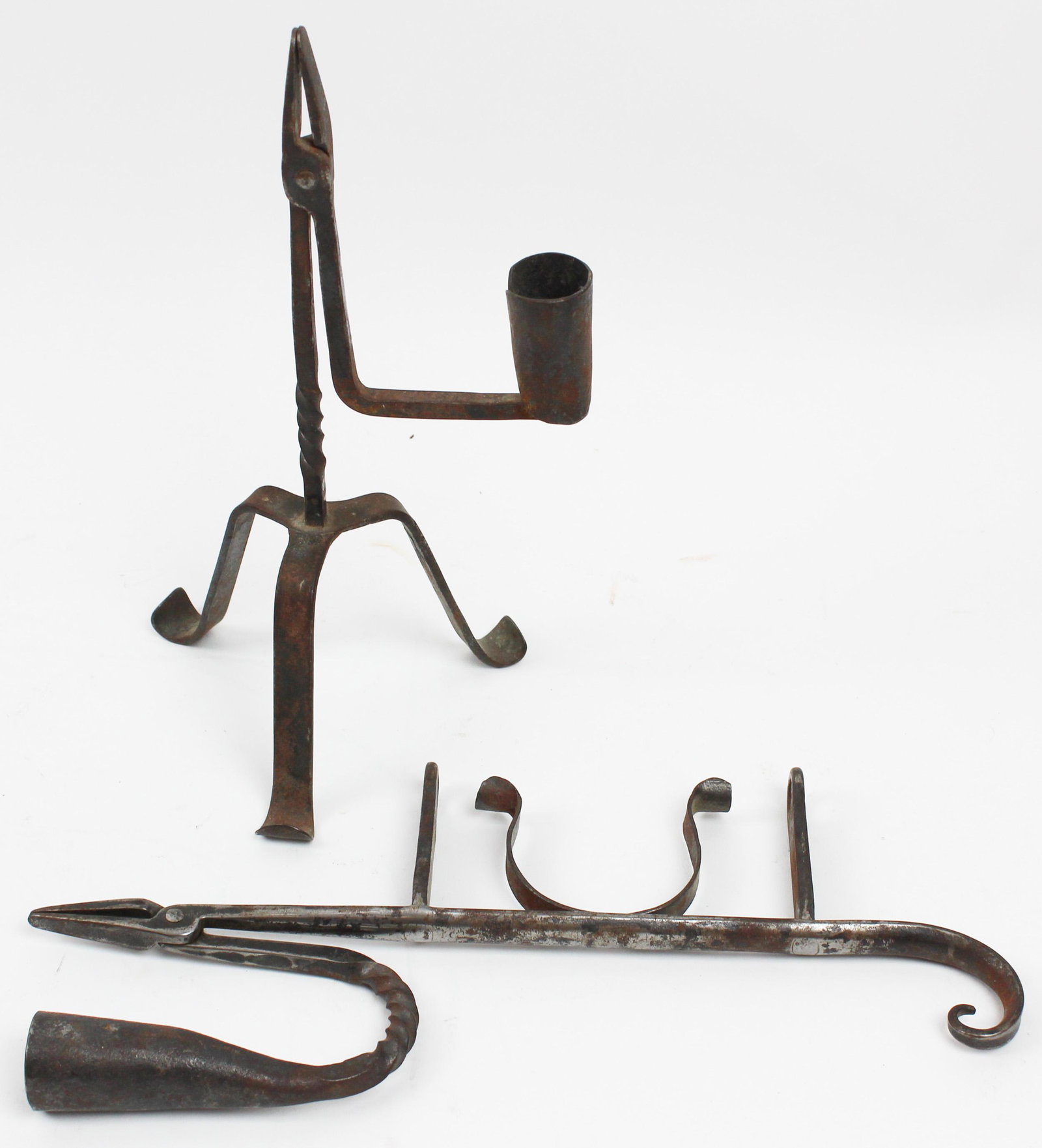 Two 18th c rush holder candlesticks: Two 18th c wrought iron rush holder candlesticks, one on three legs, the other would fasten to an upright iron rod or lamp base, hts/ lengths 10", 11 1/2"