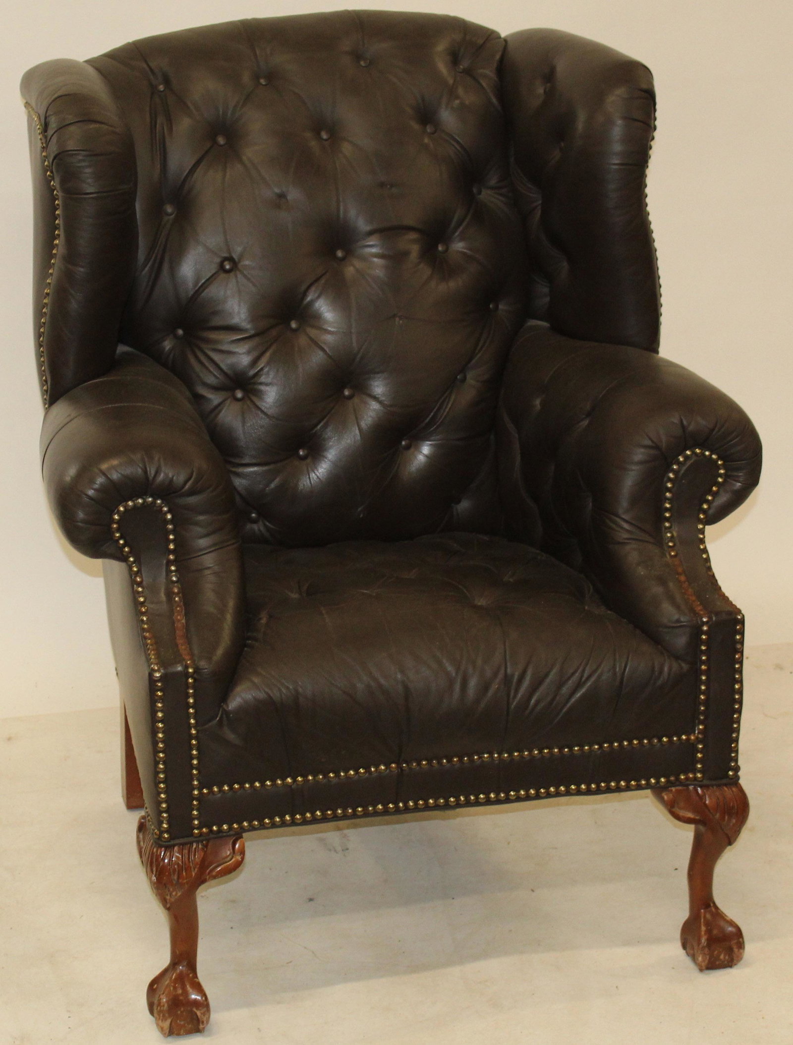 Chesterfield Wing Chair: Mid 20th Chippendale style Chesterfield brown leather and stud wing chair. Ball and claw feet. Has wear. Rust on studs, 41" h, 36" w.