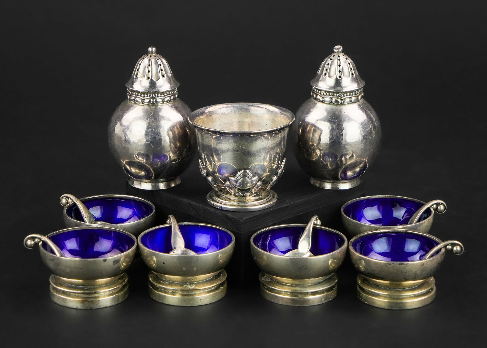 Georg Jensen Sterling Salts and Pepper Pots: A group of Georg Jensen Denmark sterling silver tableware including a pair of handwrought pepper pots, an "Acorn" pattern footed master salt, and a fine set of individual footed salts with cobalt blue