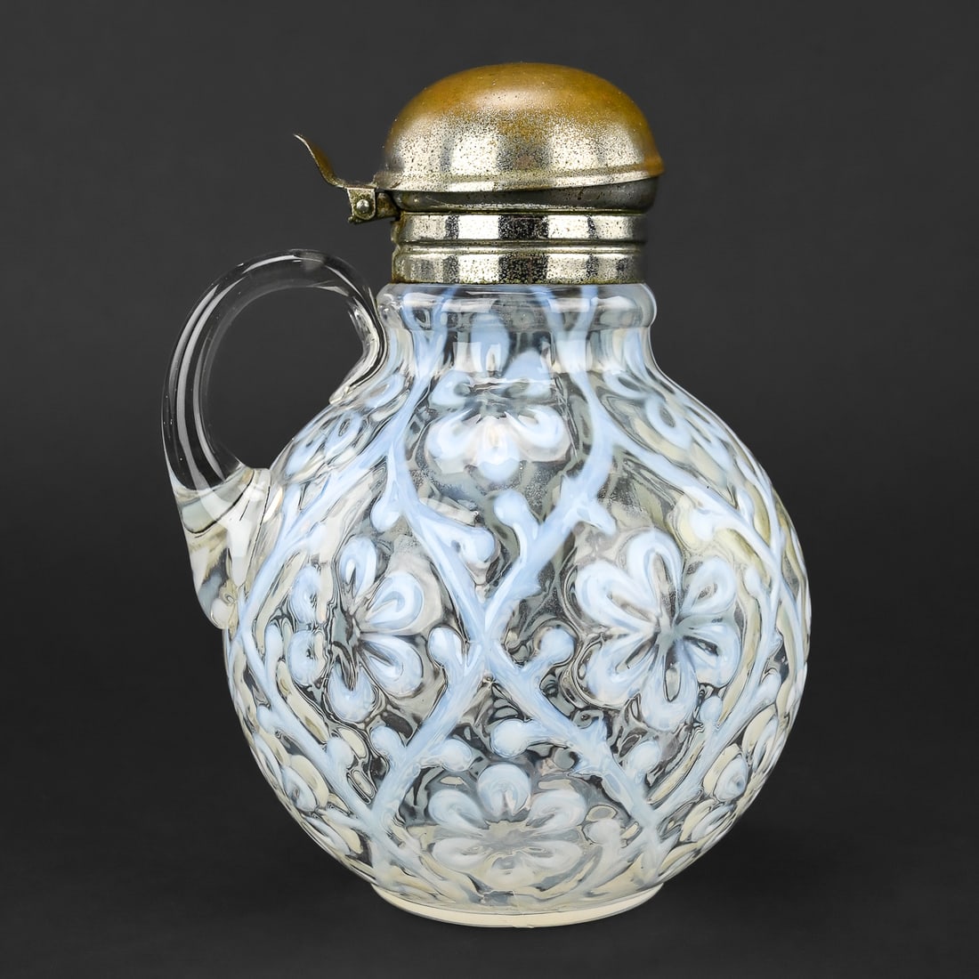 Northwood White Opalescent Spanish Lace Pattern Syrup Pitcher: Late 19th century Northwood glass syrup pitcher featuring white opalescent glass with the Spanish Lace pattern. Fitted with a hinged metallic lid. Approx. 6" H x 5" W.
