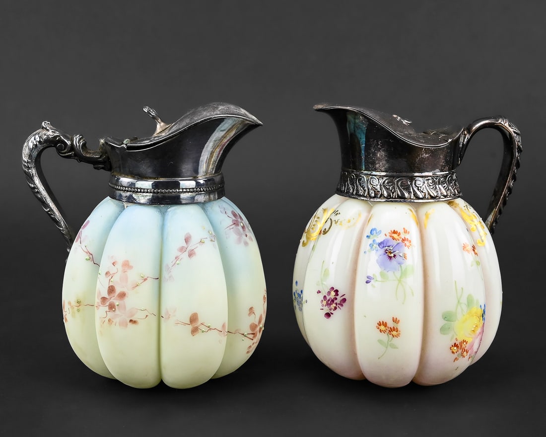 2 Milk Glass Syrup Pitchers with Sterling Plate Lids: Pair of milk glass syrup pitchers, one with a glossy glazed finish and the other with a matte opaque surface. Both feature hand-decorated floral designs and sterling plate lids. Each measures approxim