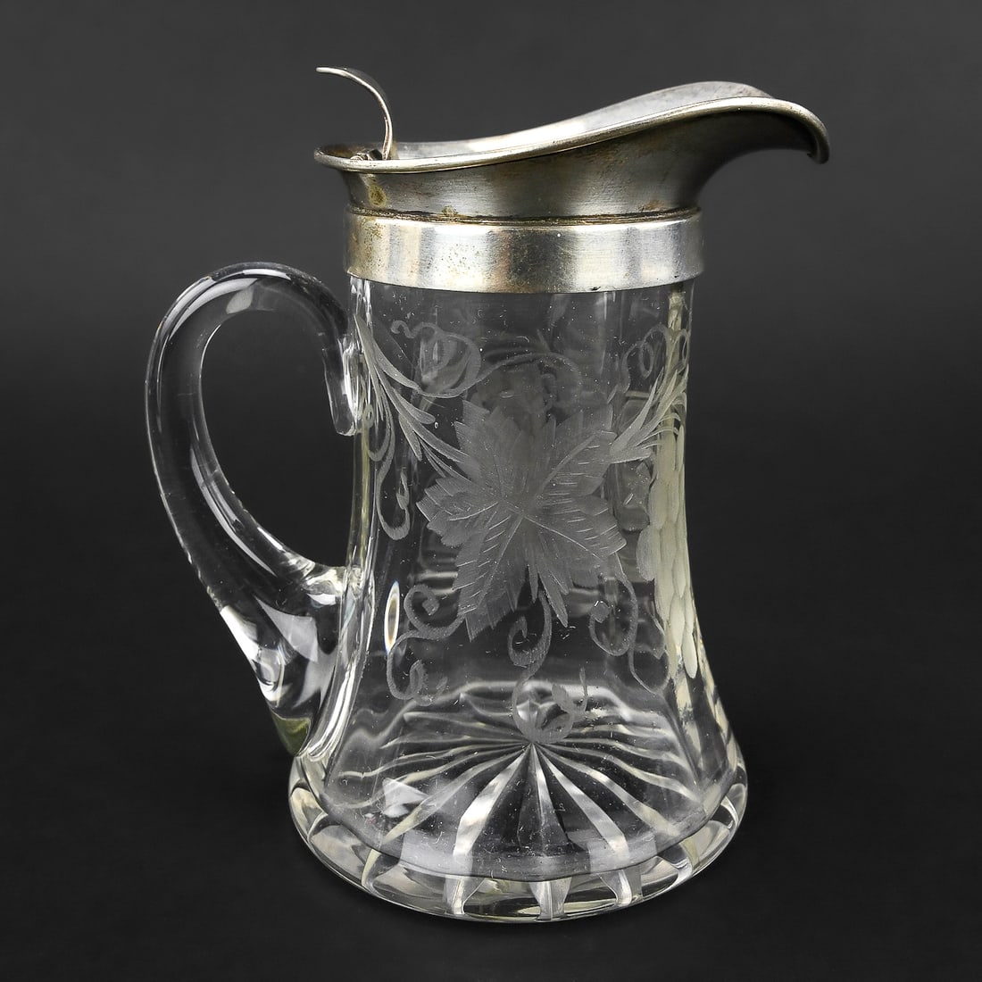 Merrill Glass Co. Syrup Pitcher with Sterling Lid, c.1922–1931: Etched glass syrup pitcher by Merrill Glass Co., dated between 1922–1931. Decorated with grape and floral motifs, and marked “692.” Topped with a sterling silver lid. Measures approximately 