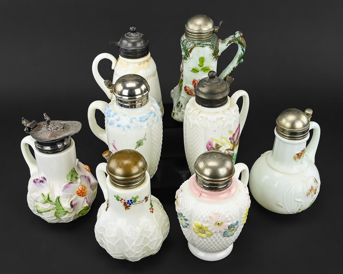 8 Hand-Painted Milk Glass Syrups & Creamers: Group of 8 milk glass syrup pitchers and creamers, most with hand-painted floral decoration and metal lids. Includes one attributed to Consolidated Glass Co., one with a silver-plated lid, and the rem