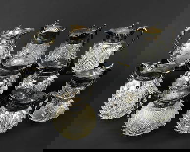 10 Cut Glass Syrup Pitchers w/ Silver Lids: Group of 10 cut glass syrup pitchers with silver-plated lids. Patterns include fern and fan, diamond cut, medallions, cross hatched diamonds, and floral daisy-like motifs with grass. Sizes range from