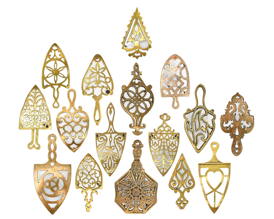Brass Trivets (16 Pieces): Group of sixteen vintage brass trivets, similar in size and quality, some featuring heart-shaped decorations. Largest measures approx. 9" L x 4" W. Retain original patina and light age-appropriate wea
