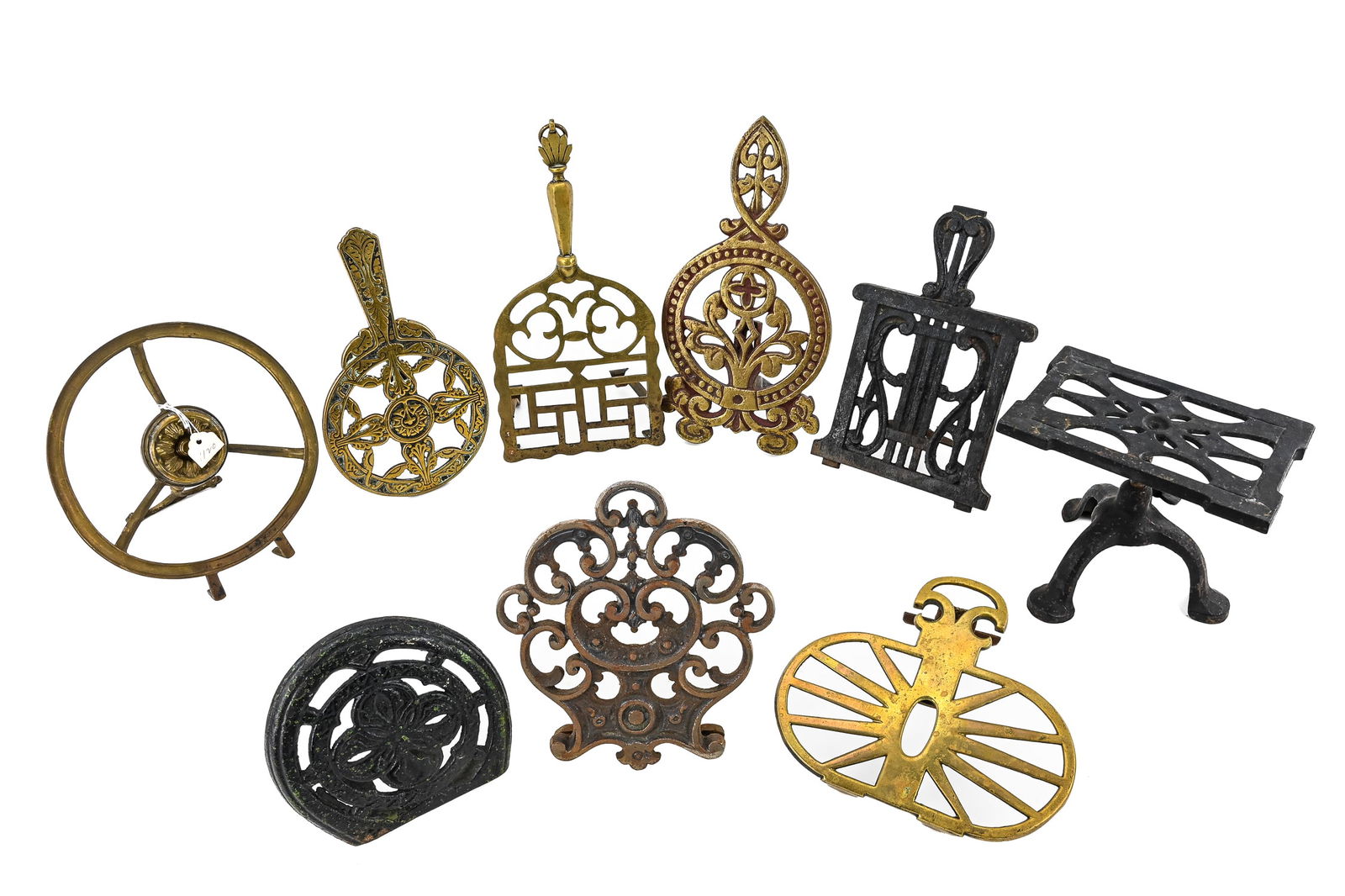 Decorative Brass and Cast Iron Trivets (9 Pieces): Group of nine decorative trivets, mostly brass with some cast iron, all featuring attached stands. Largest measures approx. 11" x 5". Retain patina and age-appropriate wear.