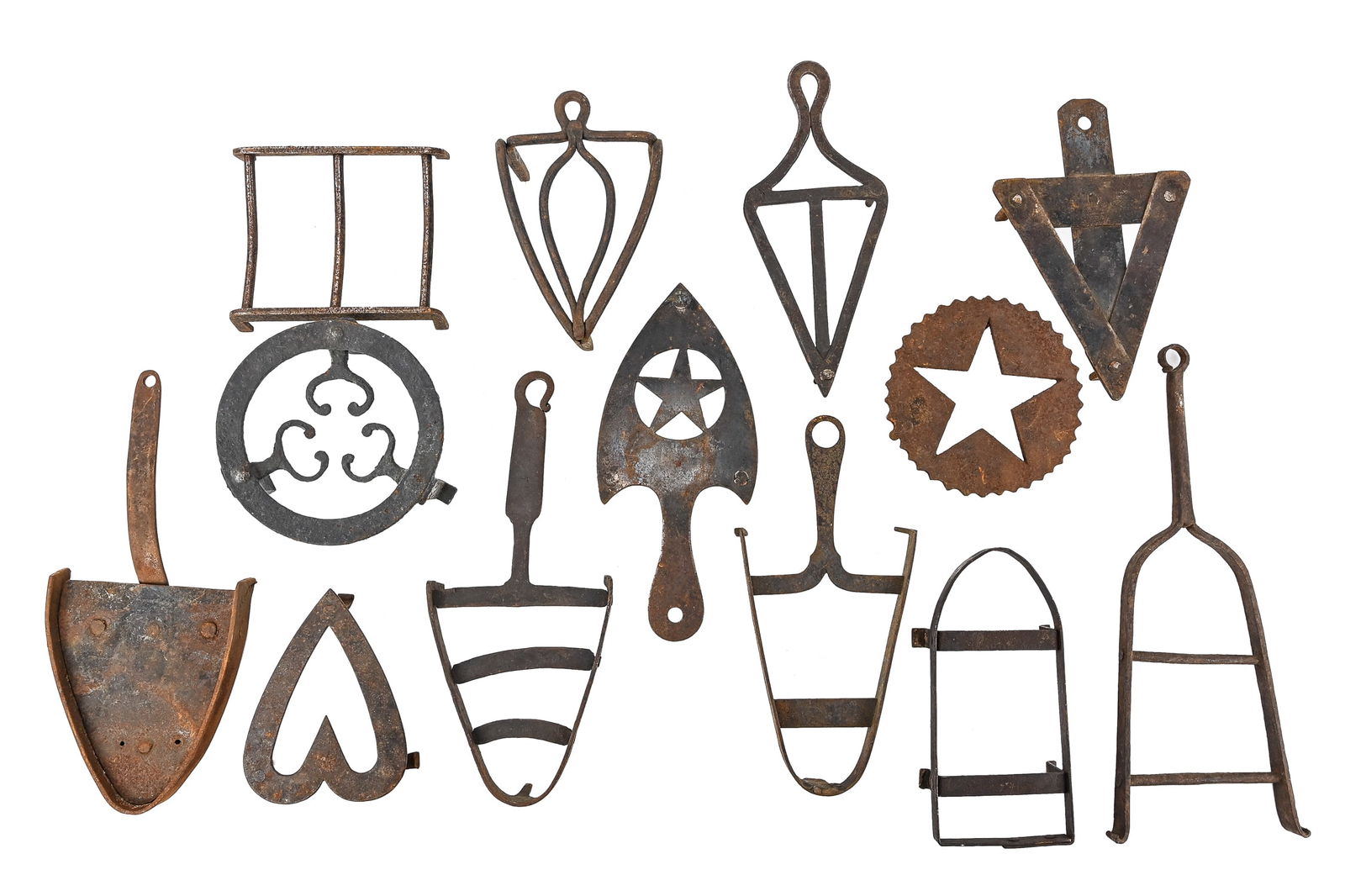Early Cast and Wrought Iron Trivets (13 Pieces): Group of thirteen early cast and wrought iron trivets featuring decorative motifs such as stars and hearts, as well as attached handles. Shapes include circles, shield/horse-shoe forms, and triangles.
