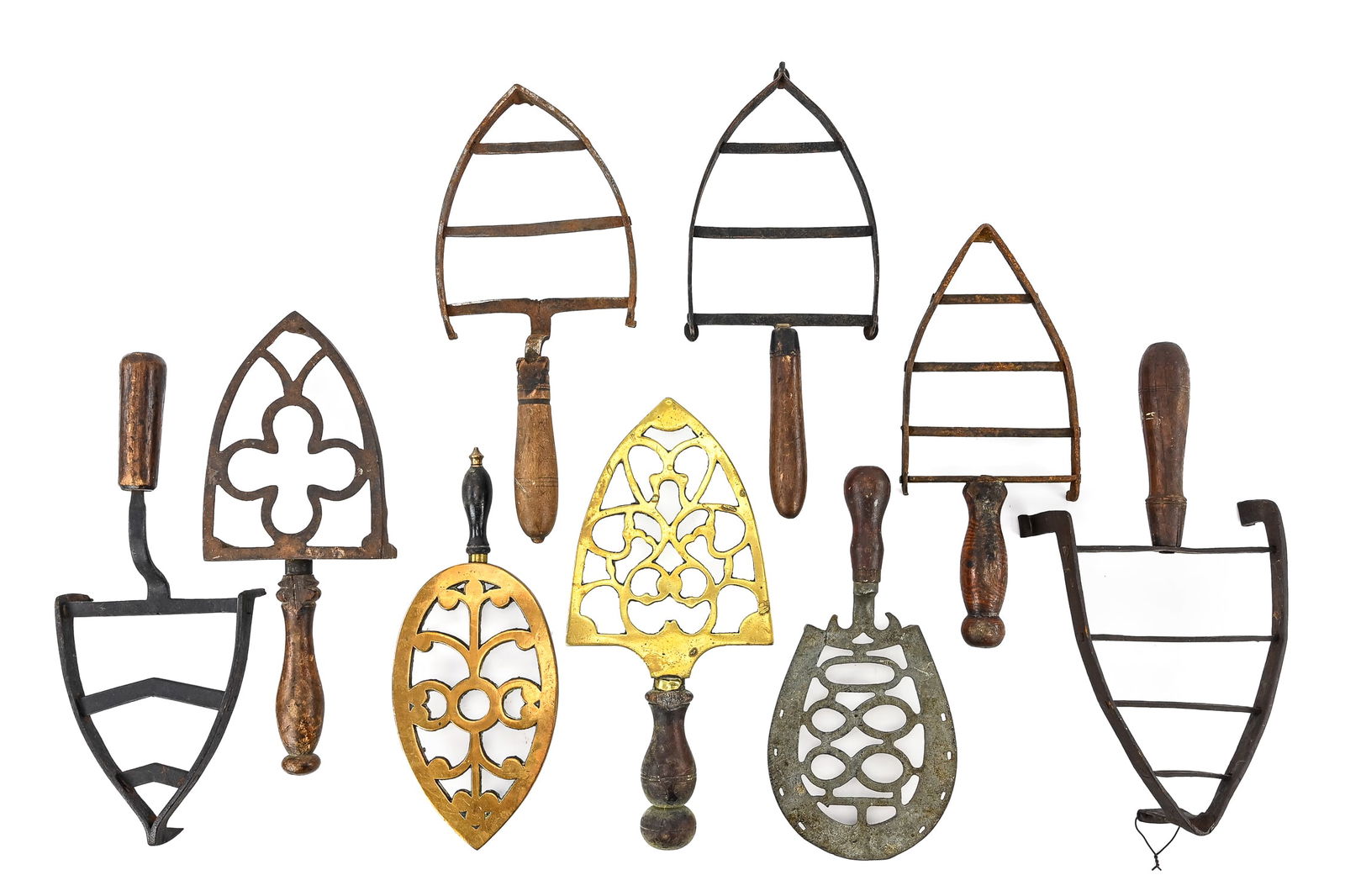 Cast Iron and Brass Trivets with Wooden Handles (9 Pieces): Group of nine cast iron and brass trivets, all featuring wooden handles. Most have perpendicular bars for supporting pans, while others display decorative patterns, including a four-leaf clover design
