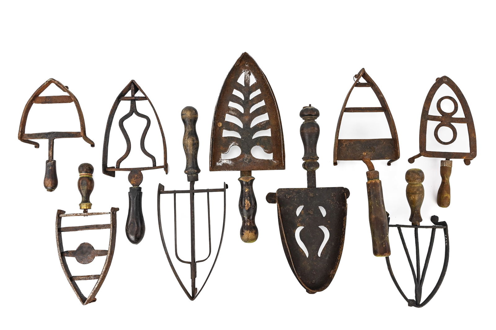 Group of 9 Cast Iron Trivets with Wooden Handles: Nine cast iron spade-shaped trivets, each with three legs and wooden handles. Largest measures approx. 12" L. All show some surface corrosion. Estimate: $100–$150.