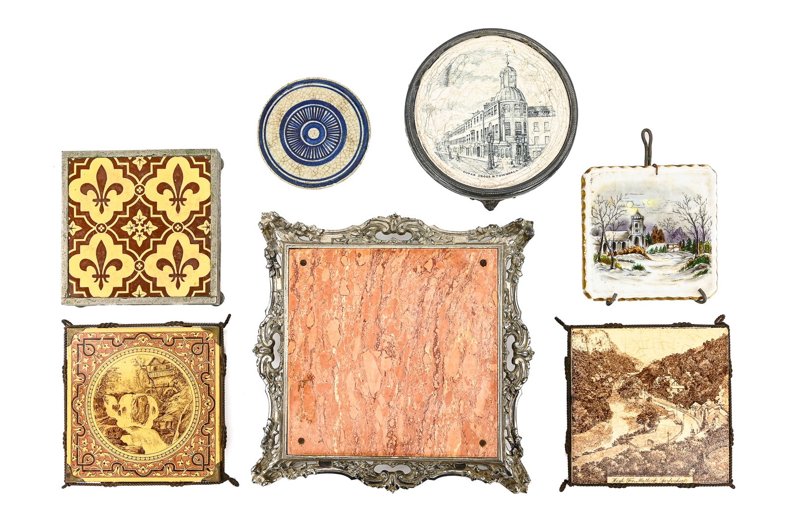 Group of 7 Saddle-Style Tile Trivets with Stands: Seven saddle-style tile trivets with stands, including three Minton China examples featuring houses, streams, waterfalls, and fleur-de-lis motifs; a winter church scene at night (unmarked); a blue cir