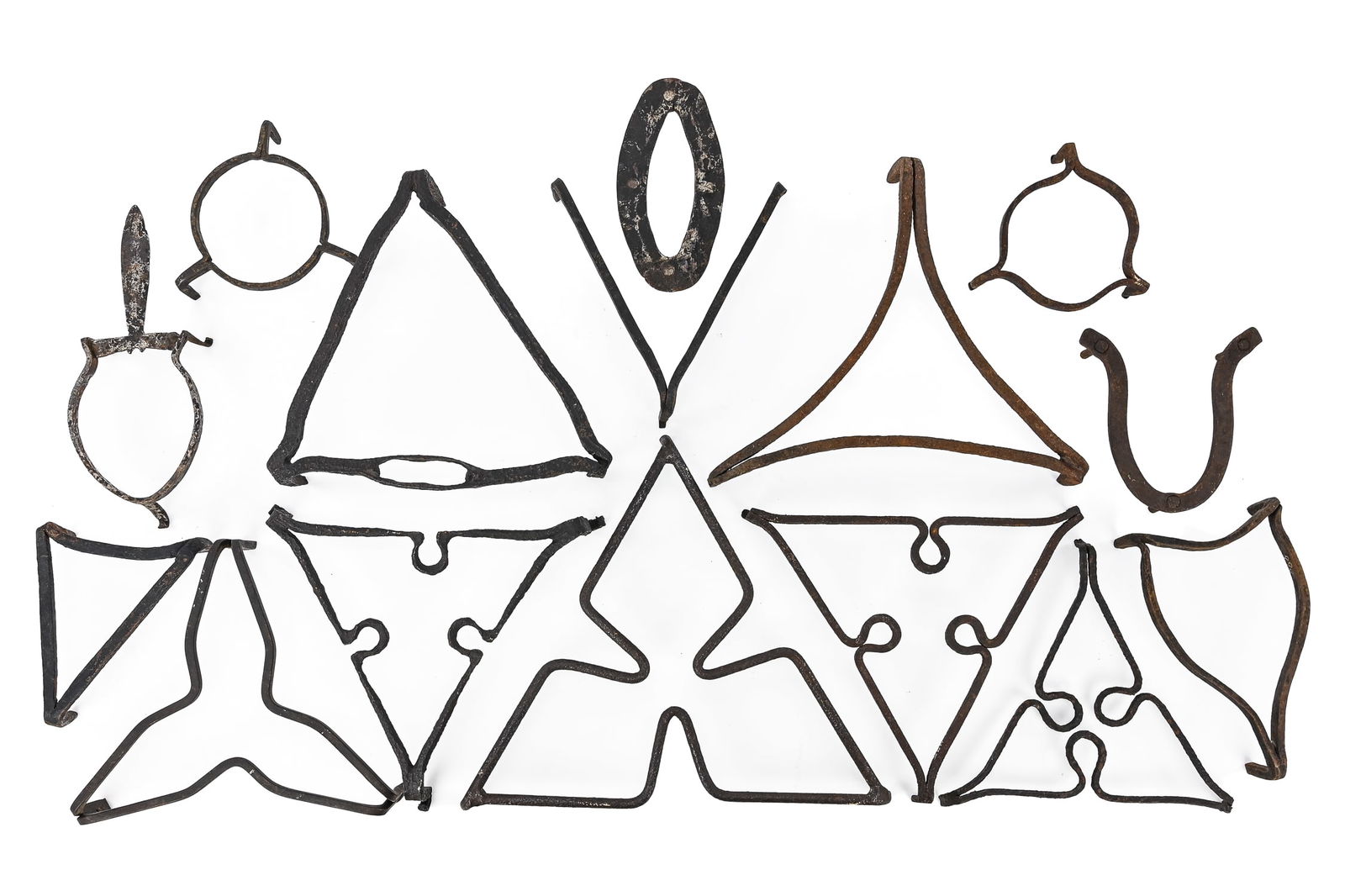 Group of 15 Wrought Iron Triangular Trivets: Fifteen triangular wrought iron trivets, most with three feet and exhibiting the hammered texture characteristic of hand-forged pieces. Largest trivet is triangular with pinched sides, measuring appro