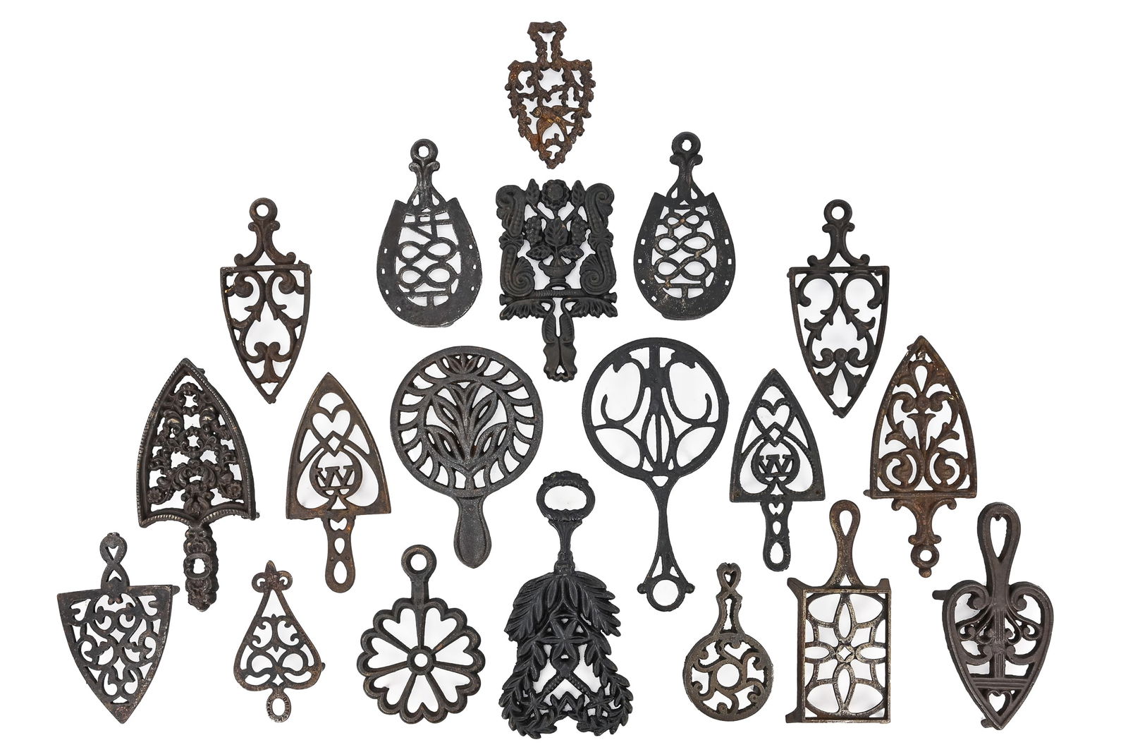 Group of 19 Cast Iron Trivets: Nineteen cast iron trivets, some marked British, mostly spade-shaped with a few horseshoe- and circular-shaped examples. Several have handles. All measure approx. 9" L