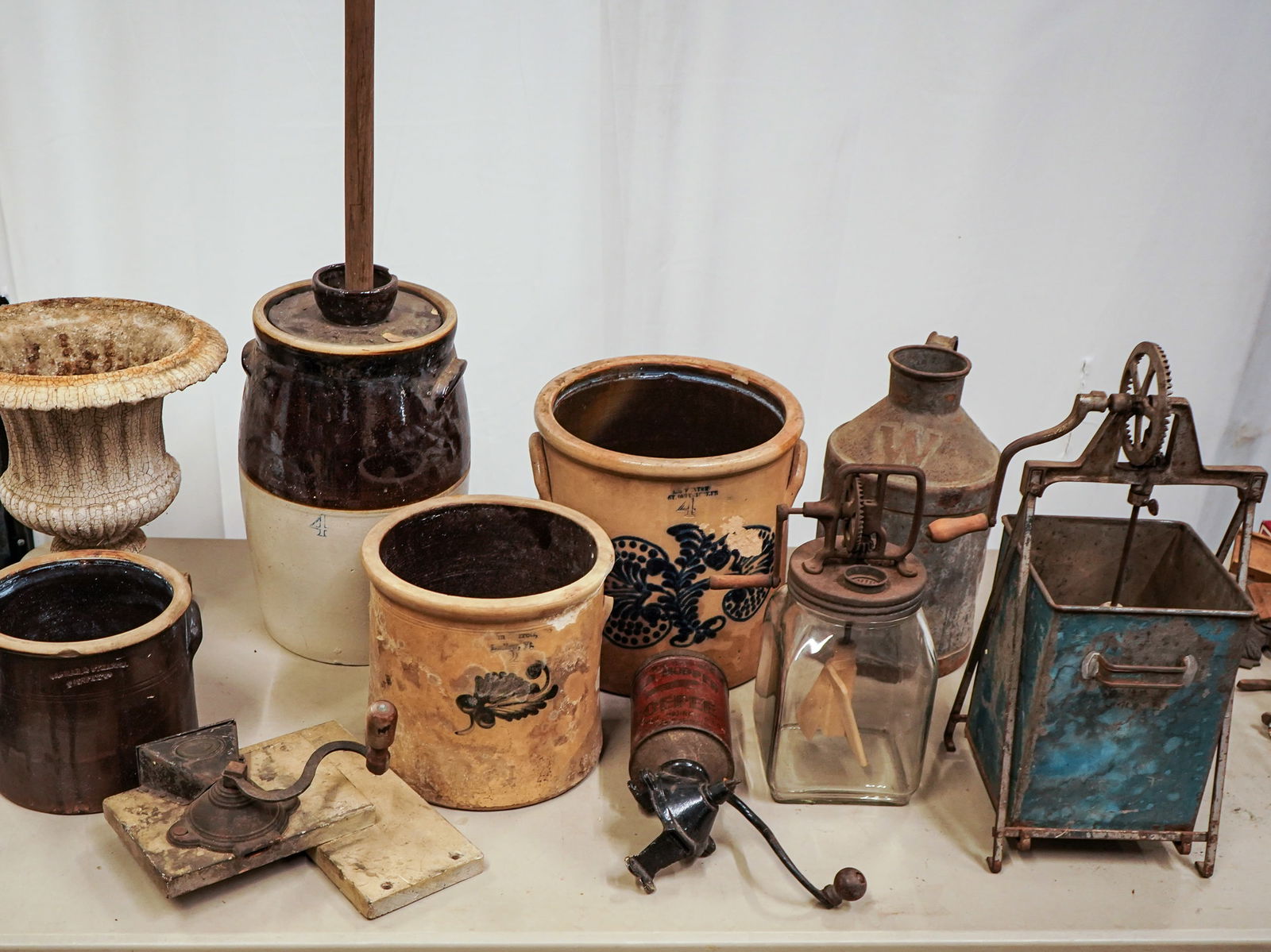Kitchen and Stoneware Table Lot: Butter churns, stoneware, cast iron garden urn, coffee grinders, cream can (local pick-up/ private carrier required)