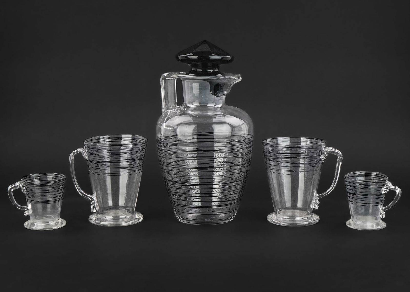 Steuben Threaded Cocktail Pitcher and Mugs: Steuben Carder era blown art glass cocktail pitcher with black onyx glass stopper and applied threaded decoration to mugs 2.75"-11" -some losses to threading one one small mug