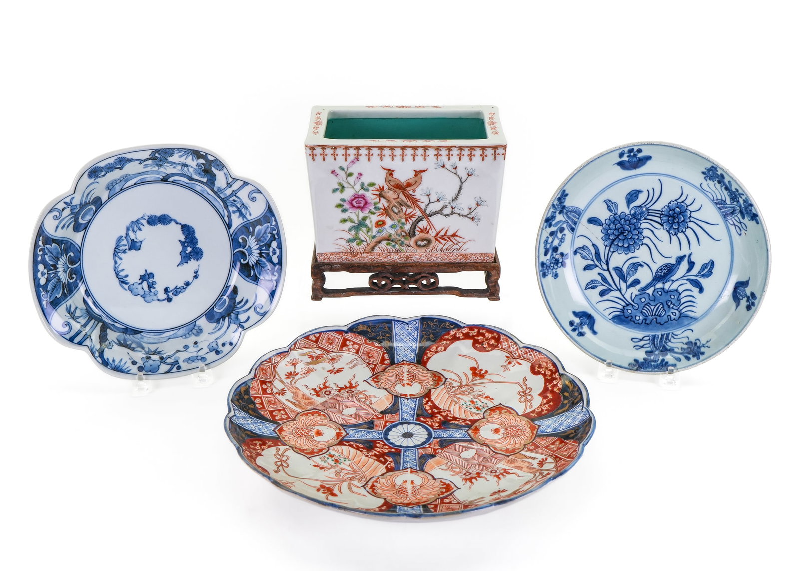 Four Decorative Asian Porcelain Items: Group of four decorative Asian porcelain items including Chinese Famille Rose cache pot planter on carved wooden pedestal, Japanese Imari fluted dish, and two Chinese blue and white dishes, one with o