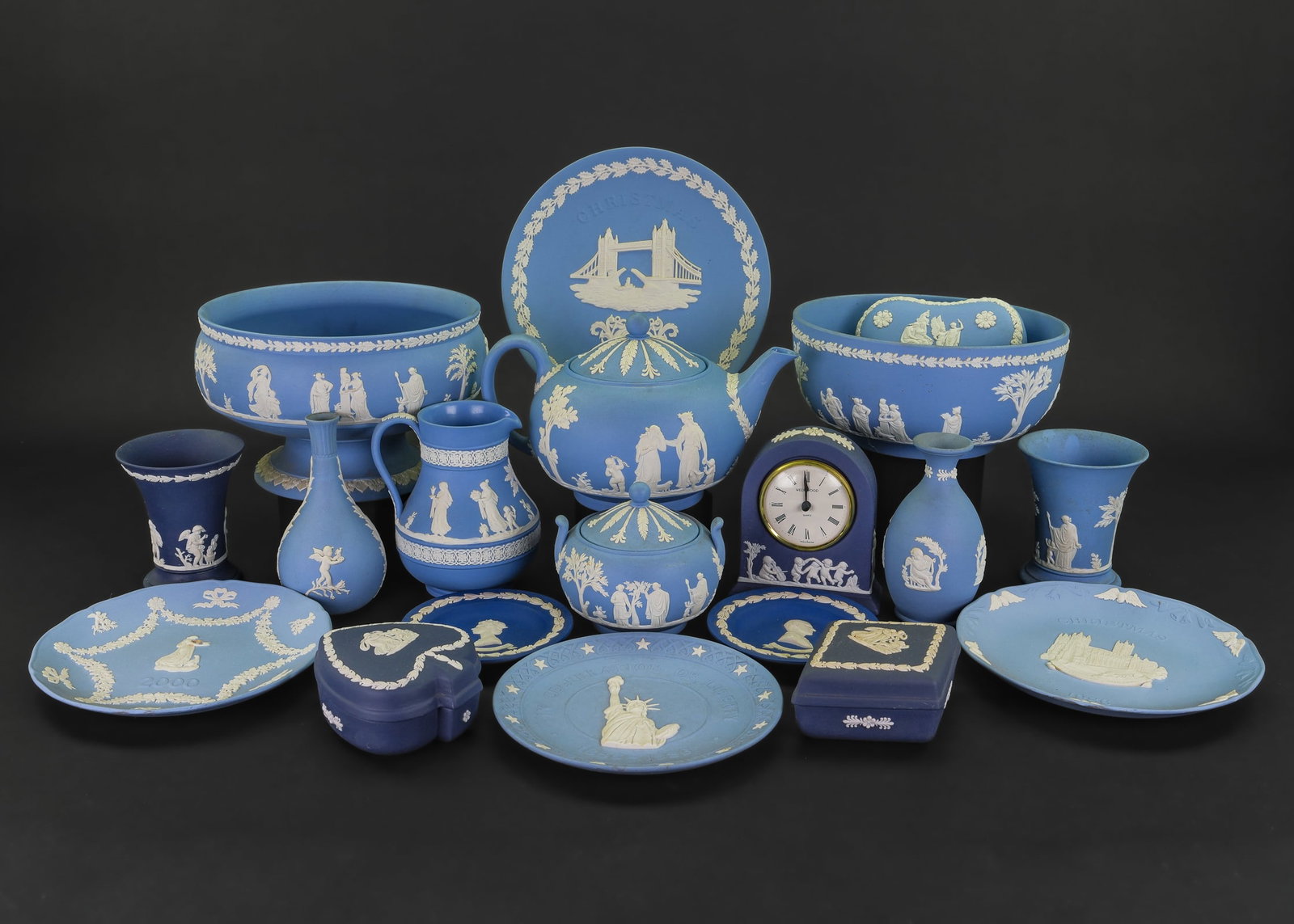 19 pcs. Wedgwood Solid Blue Jasperware: Collection of 19 pcs. Wedgwood solid blue jasperware including 2 centerpiece bowls, Etruscan jug, dresser boxes, vases, desk commemorative plates clock, etc.-some pieces in need of cleaning, teapot ha