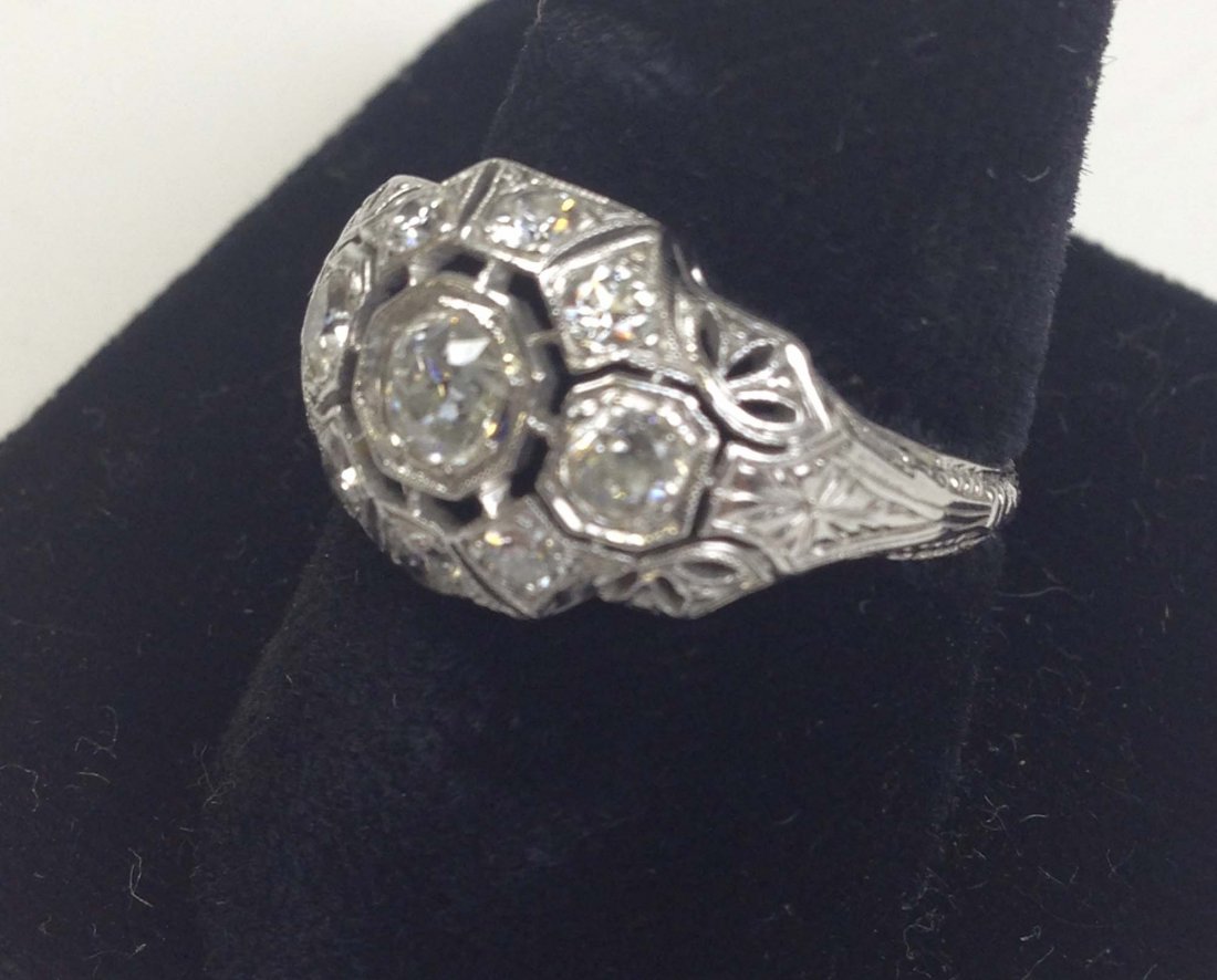 Edwardian white gold cocktail ring having center ? ct.: Edwardian white gold cocktail ring having center ? ct. round cut diamond in octagon bezel frame surrounded by 6 smaller diamonds in bezel sets each with openwork surrounds.
