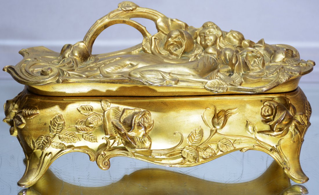 Art Nouveau Style Jewelry Box: Art Nouveau style jewelry box with reclining nude woman resting in flowers on top of hinged lid with footed base. Marks: signed W-B on bottom Dimensions: 6"t x 11"w x 5"d Date: Ca. 1900