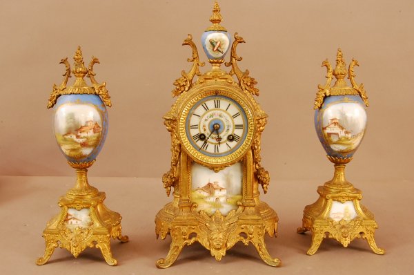 3 Pc. French Serves Clock Set. Floral Painted Por: 3 Pc. French Serves Clock Set. Floral Painted Porcelain dial, Scenic Panel, Cherub faces on base & sides. Decorated porcelain finial, Clock is 14"t x 7"d x 5"d : 2 matching urns have scenic painted pa