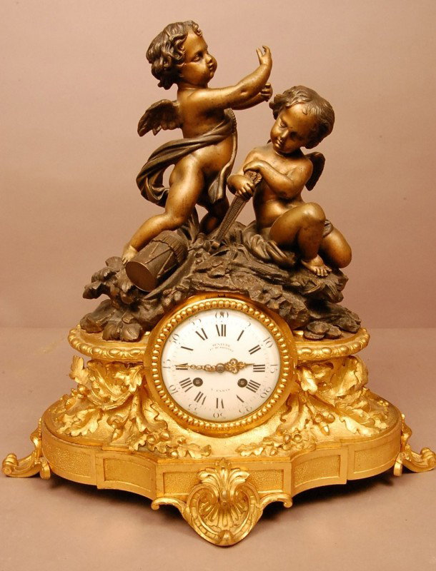 French Louis XV style Bronze mantel clock with 2 ch: French Louis XV style Bronze mantel clock with 2 cherubs resting on top of Dore Bronze base of leaf & acorn design. Porcelain dial with Roman numerals. Signed Denlere FT De Bronze A. Paris 16" t x 16"
