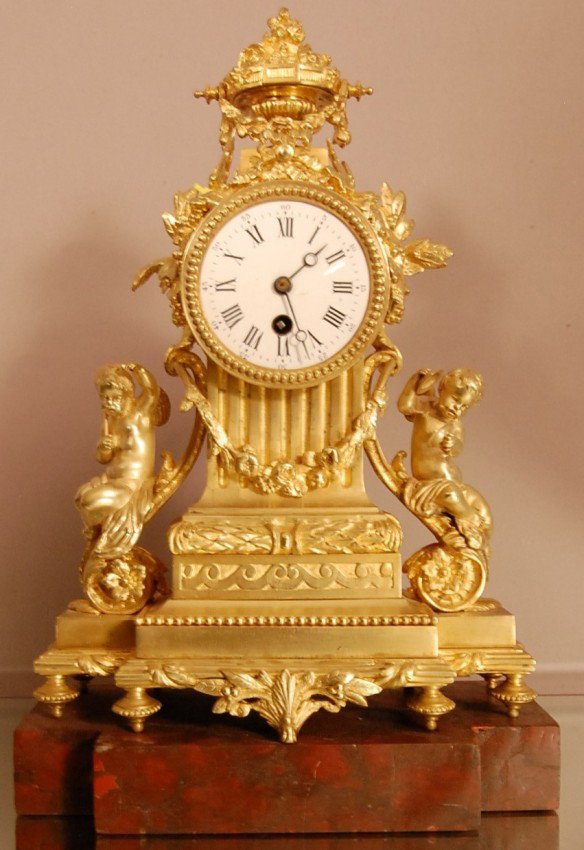 French Dore Bronze Louis XVI style Figural mantel : French Dore Bronze Louis XVI style Figural mantel clock with flowers. Urn shaped finial mounted on top of clock. Pair of musical cherubs sitting on each side of clock. Porcelain Dial mounted on marble
