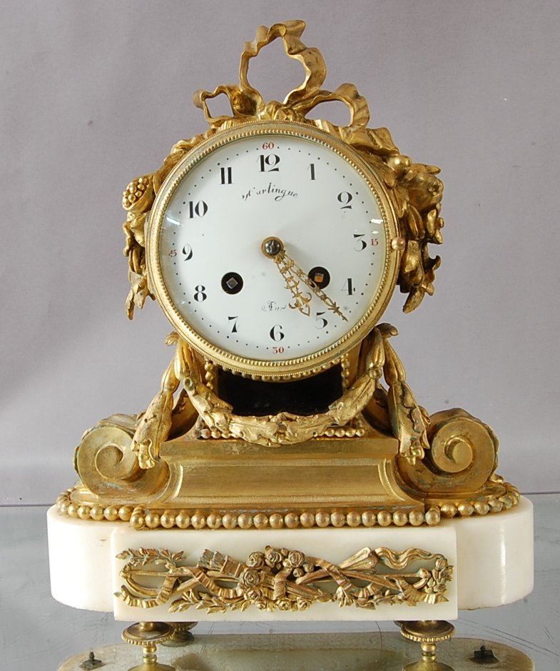 French Dore Bronze Louis XVI style Mantle Clock: With Ribbon crest decorated sides on marble base. Porcelain dial, time & strike, silk string movement. 12" t x 10" w x 4" d . CA. 1860