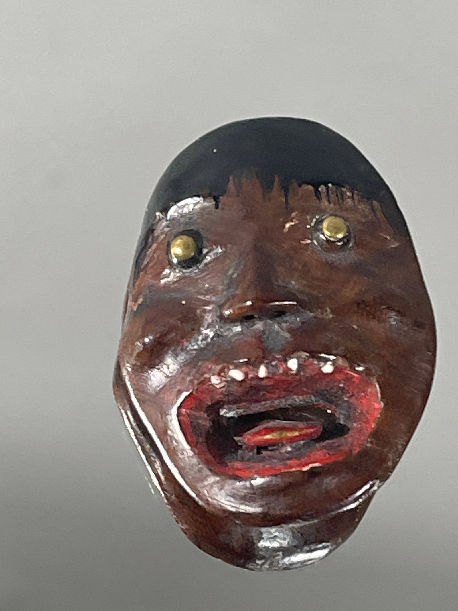 An Unusual Lacquered Wood Reversible Mask Netsuke of a Monstrous Head: The wood mask netsuke lacquered in brown, black and red. The front showing a screaming face with gilt-brass eyes, a black-lacquered boyish head of hair, and the opened mouth lacquered in red with a vi