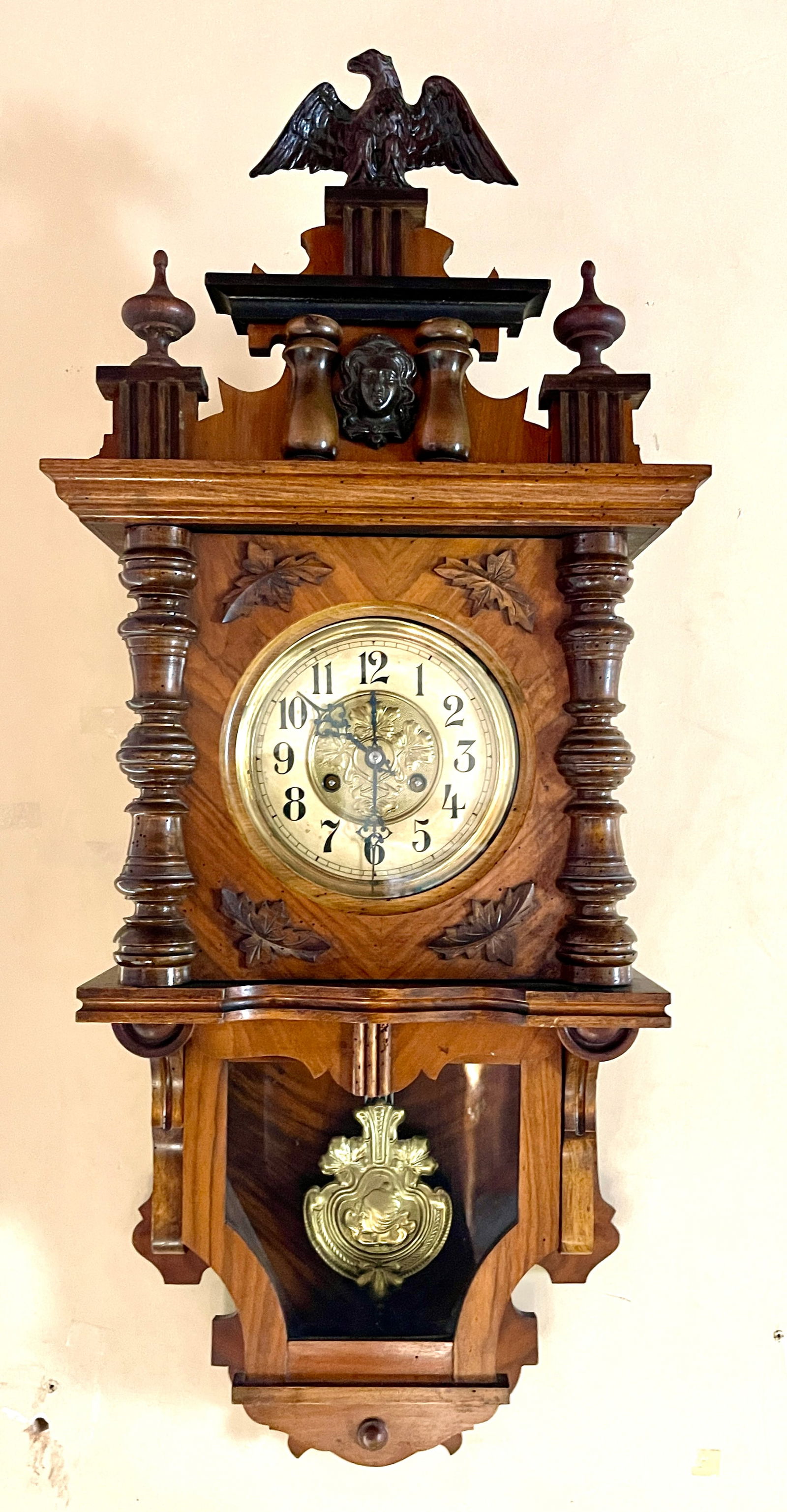 German Free Swing Wall Clock: German walnut and oak enclosed free swing wall clock. Eagle in crest, oak leaf, brass 6"dial, Beautiful ladies bust, clock is complete and running. German, 37"t x 8"d x 16"w, circa 1900.