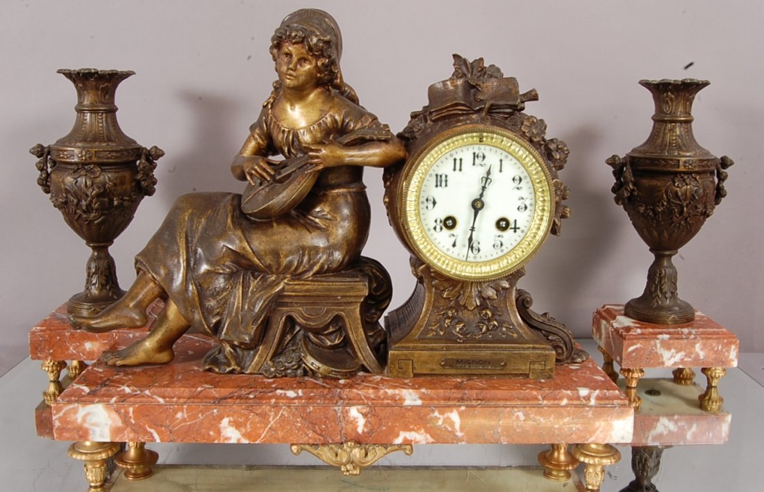 French Louis XVI 3 pc. Figural clock set: With spelter statue of lady Mignon by Moreau seated next to clock. Porcelain dial. Time & bell strike with 2 matching urns. Works signed P. Clock is 13" t x 16" w. Urns are 12" t. Ca. 1880