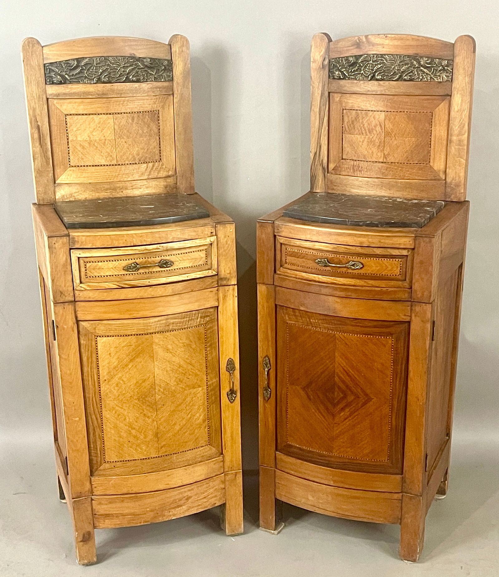 Pair of French Marble Top Side Cabinets: Walnut with floral decorated bronze mounts and marble tops. One drawer, one door with bow front marquetry panels. DIMENSIONS: 47"t x 15"d x 16"w. ORIGIN: France CIRCA: 1920.