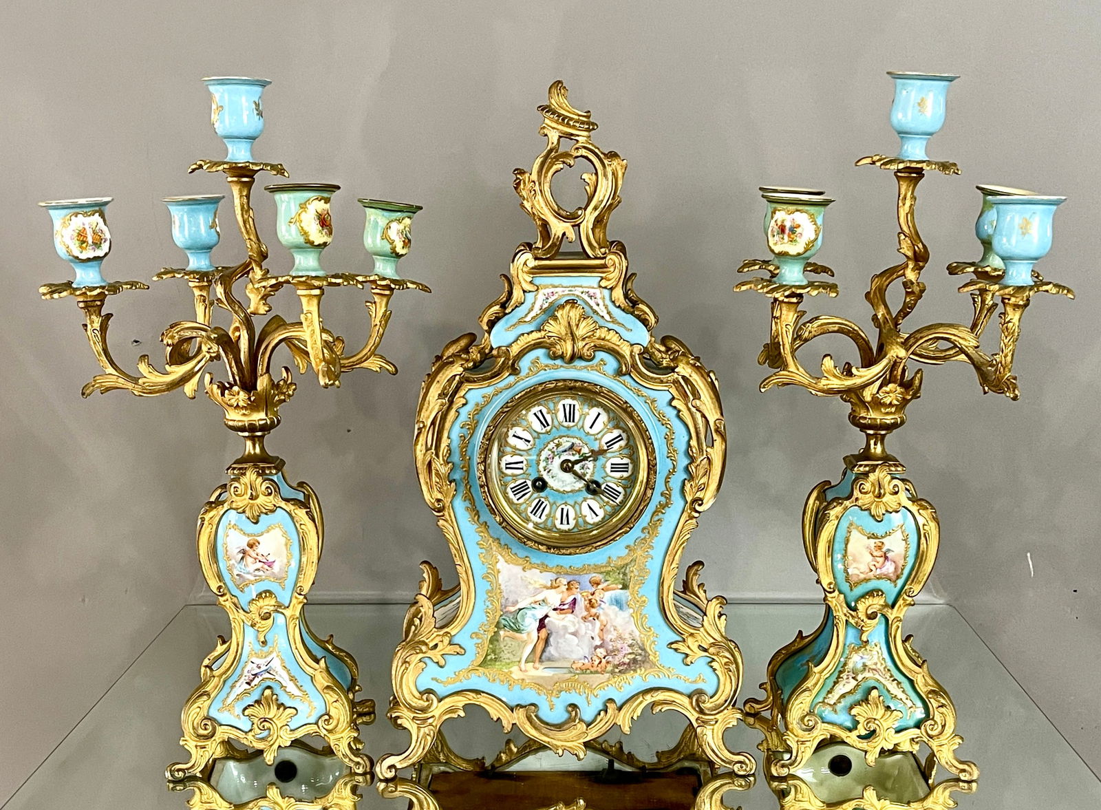 French 19th Cent. 3-Piece Porcelain Clock Set: Hand painted center panel with cherubs, matching 18" candelabras, 4" hand painted dial, with key. MARKS: artist signed CONDITION: clock is complete and in working order. DIMENSIONS: clock 19"t x 6"d