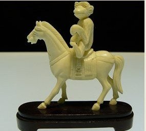 BONE SADDLED HORSE W/MONKEY: 2106B This is a tang saddled horse with a monkey riding on. It is made of Elephant Bone. It is sitting on a rosewood stand. It appears pure white in color. Very detailed carving SIZE: L: 3.5", W: 1", 