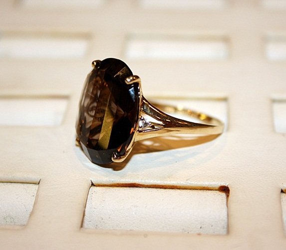 Lady's 14K Yellow Gold Smokey Quartz Ring: Lady's 14K yellow gold smokey quartz and diamond ring has 1 oval cut 4-prong set smokey quartz surrounded by 2 round cut white quartz. Total est. ct. weight of smokey quartz is 8.50 ctw. Total ring we