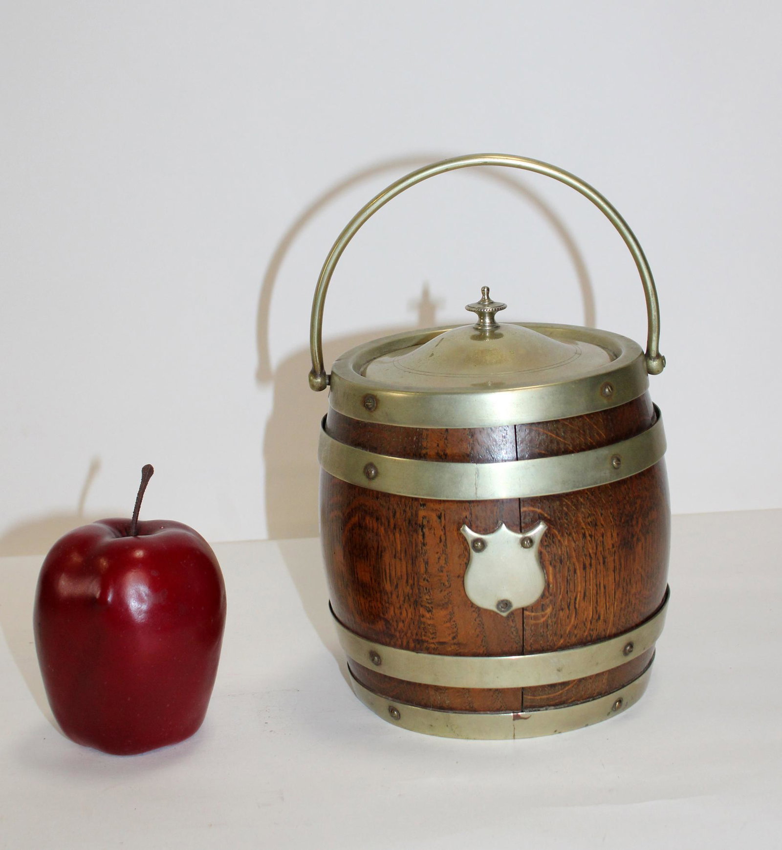 Antique English biscuit barrel in oak: Antique English biscuit barrel in oak and silverplate plate. Interior ceramic insert. Early 20th century. 7 1/2"h x 6"dia, 9 1/2"h with handle up.