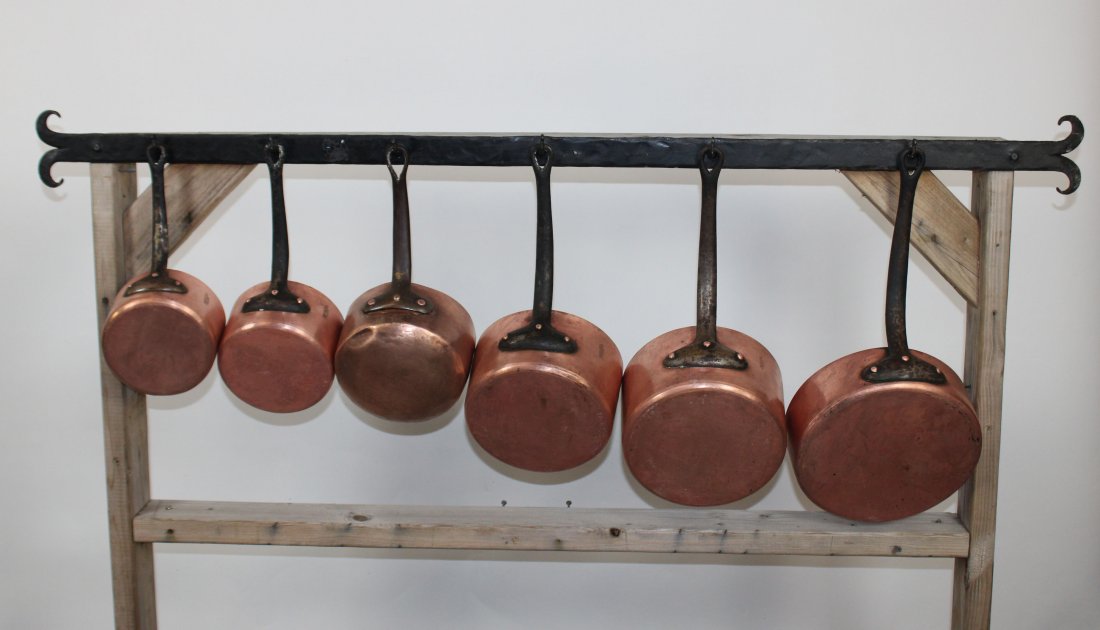 Set of 6 French copper pots on iron bar: Set of 6 French copper pots in graduating sizes. 5 pots marked Dehillerin, Paris. On hand forged iron bar. Bar is 58"l Pots range 3 1/4"-8 1/4"h x 7 1/2"-19"w. Without handles 2"-5 1/4"h x 3"-10"diam