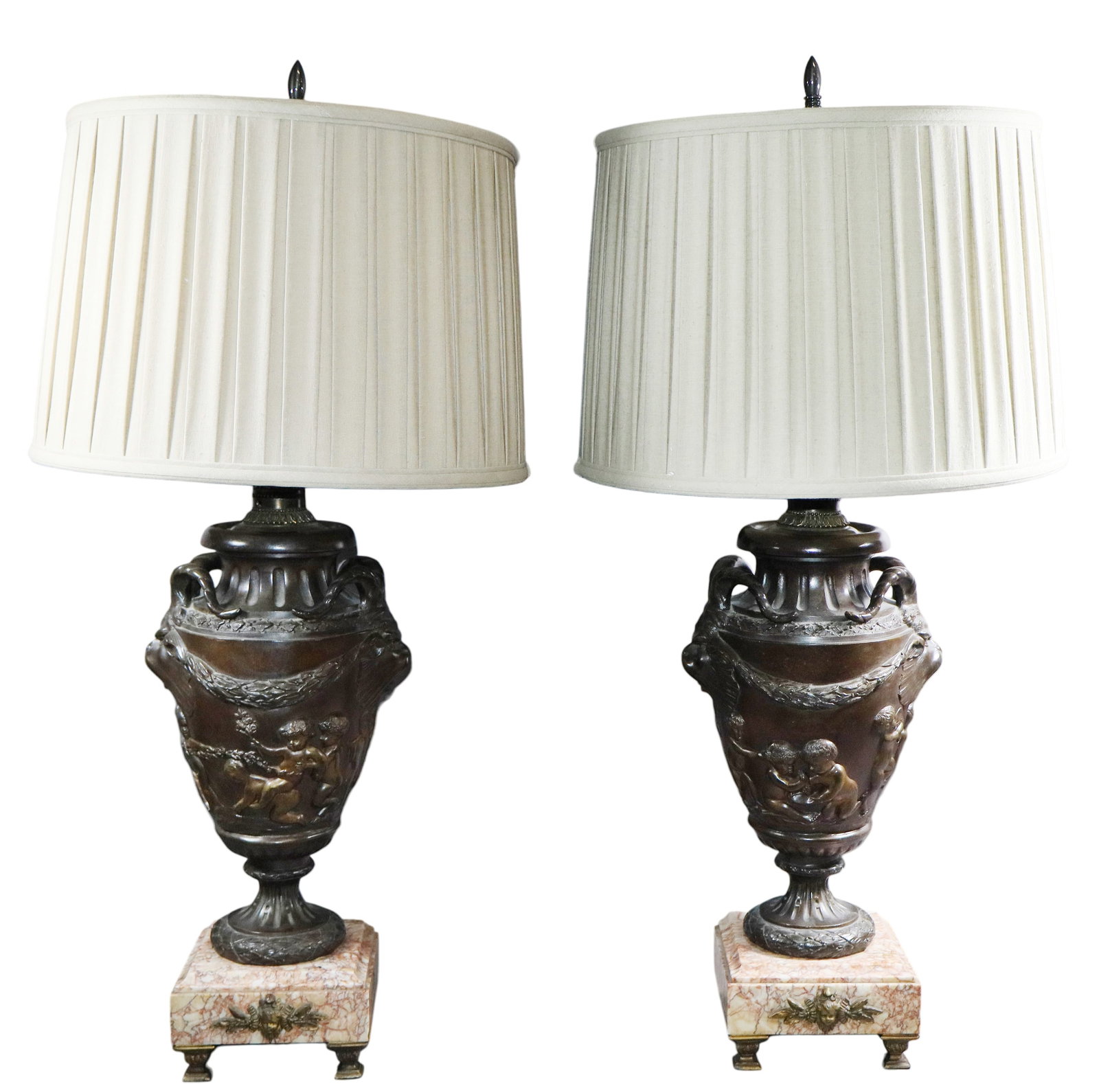 Pair of French bronze relief urn lamps with cherubs and satyr masks: Pair of French bronze relief urn lamps with cherubs and satyr masks. Lamp base: 24 1/2"h x 10"w x 6 1/2"d. Lampshade: 13"h x 14 1/4"dia. Weight: 34 lbs. total