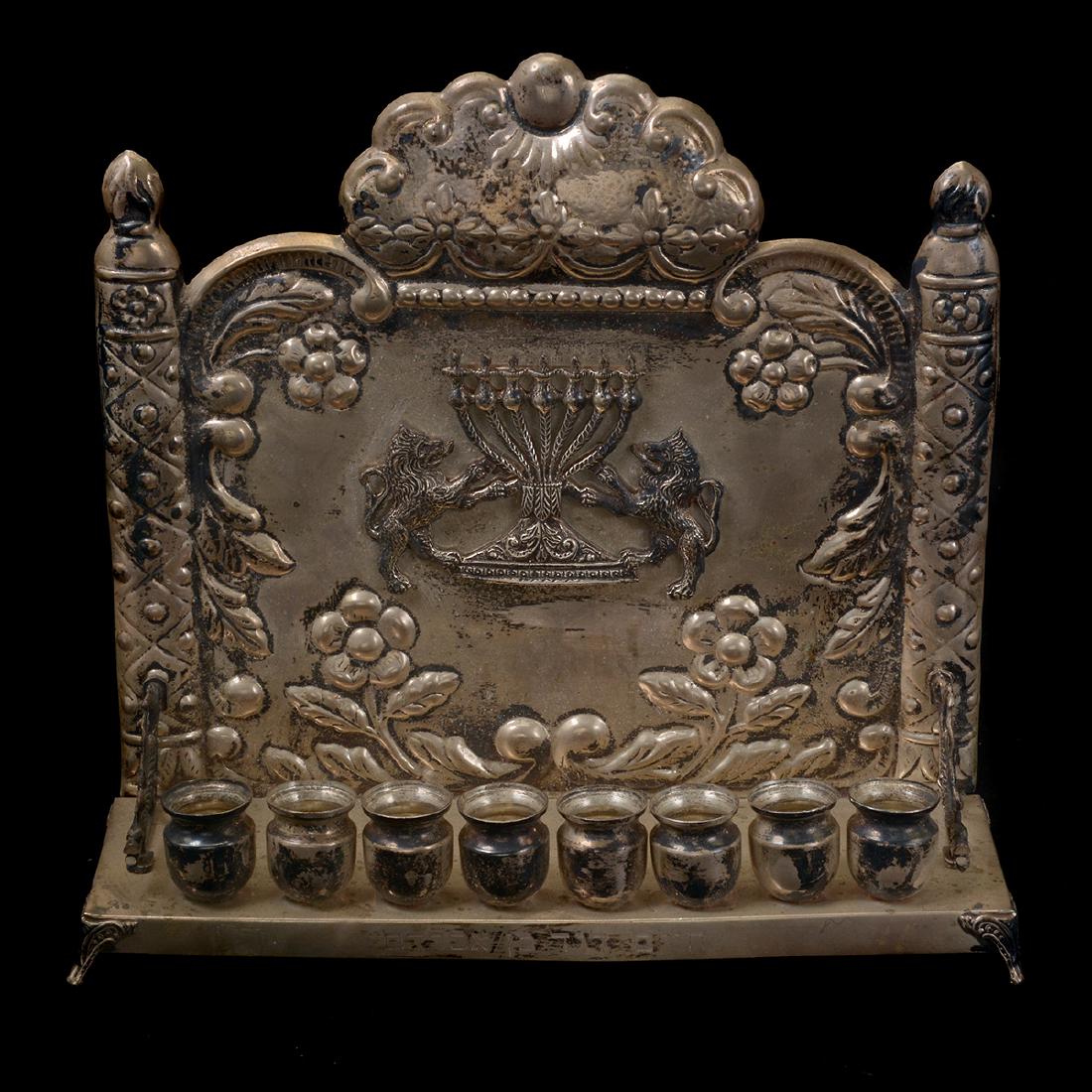 Sterling Silver Menorah: Sterling Silver Menorah. With repousse floral design, central lions, flanking columns, and candle cups on apron. {Dimensions: 10 x 10 1/4 x 3 1/4 inches. Silver weight 25.748 troy oz.}