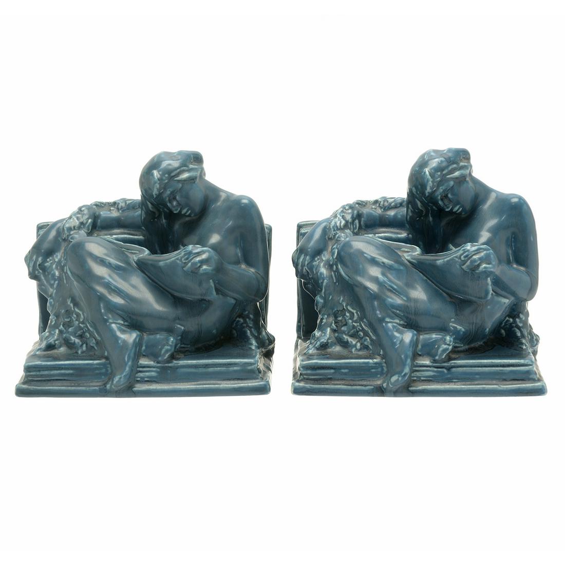 Pair of Rookwood Figural Reader Bookends #2184.: Pair of Rookwood Figural Reader Bookends #2184. Reclining reading figures set in books, with a blue glaze. Marked to underside with Rookwood mark, XXI, 2134. Cincinnati, Ohio. Circa 1920. {Approximate