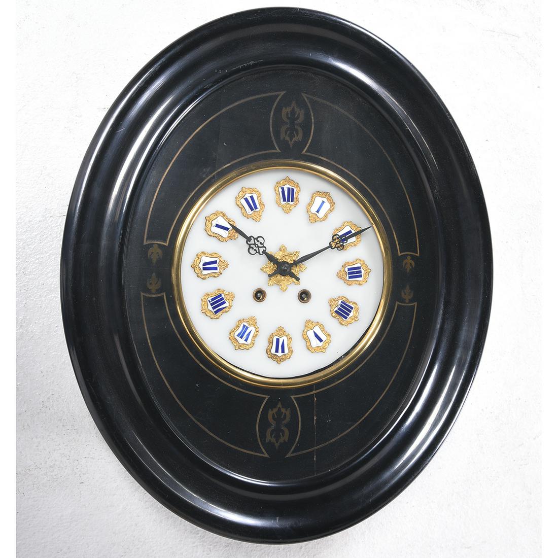 Empire Ebonized Wood Wall Clock: Empire Style Ebonized Wood Wall Clock. Milk glass dial with enameled Roman Numeral numbering and gilt metal mounts, with a brass inlaid surround, all in an ebonized oval case. {Approximate dimensions: