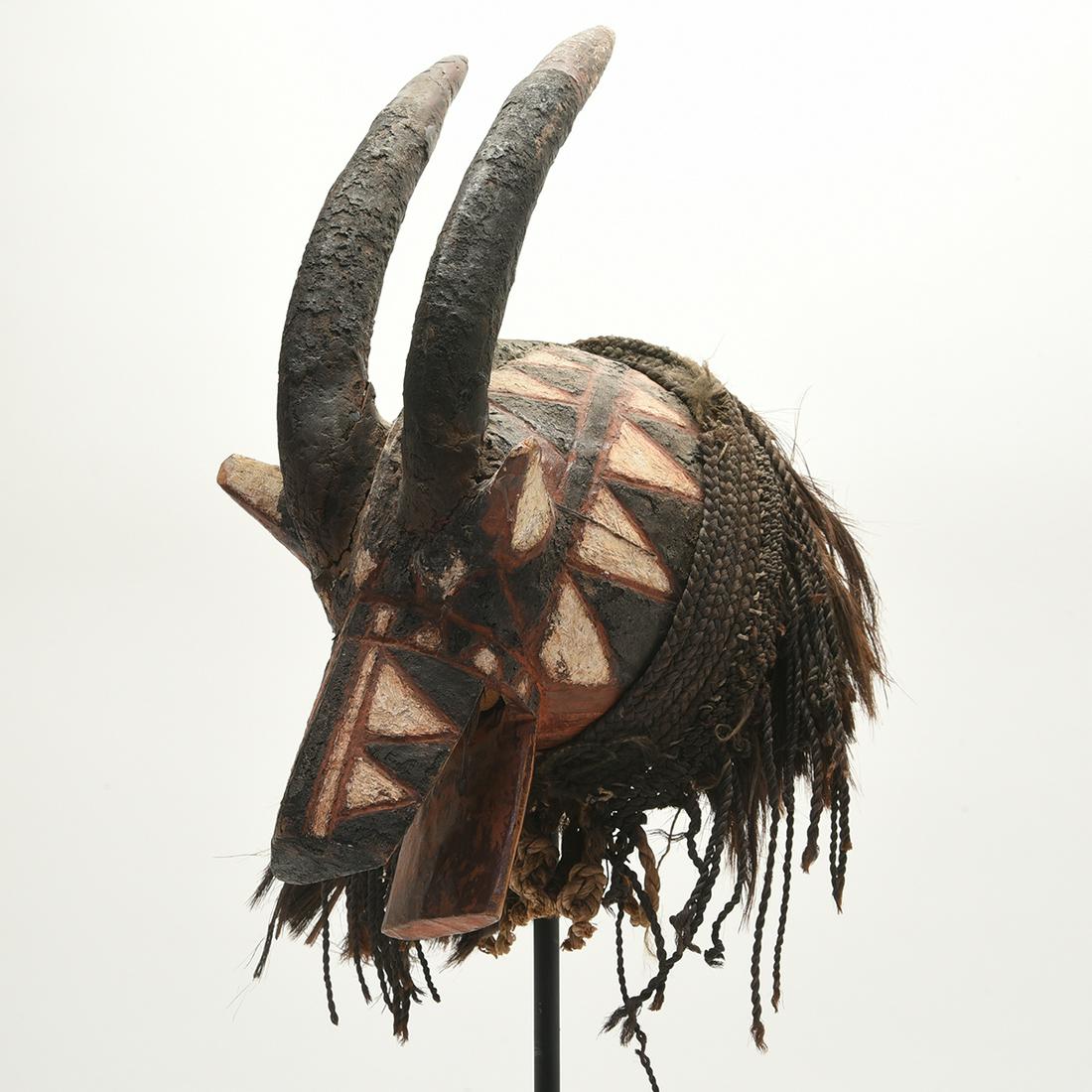 African Painted and Carved Wood Headdress.: African Painted and Carved Wood Headdress. In the form of a horned animal; painted black, red, and white; with a significant amount of animal hair attached to the back. Black metal stand included. {Ap