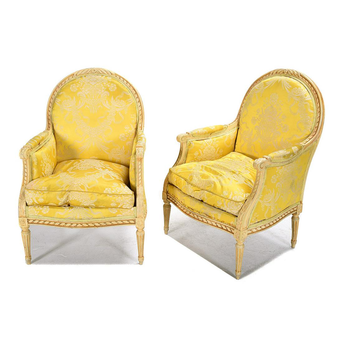 Pair of Louis XVI Style Carved and Painted Bergeres: Pair of Louis XVI Style Carved and Painted Bergeres with Silk Upholstery. The cream painted chairs with foliate and ribbon carving to frame, and tapering fluted feet. Upholstered in yellow silk floral
