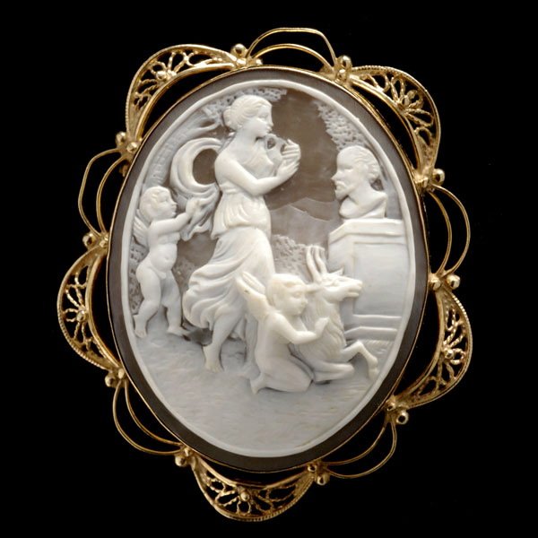 SHELL CAMEO, 14K YELLOW GOLD PENDANT BROOCH.: SHELL CAMEO, 14K YELLOW GOLD PENDANT BROOCH. Featuring one oval shell cameo measuring approximately 45.00mm x 36.00mm, depicting a woman, two cupids and a goat, bezel set in a 14k yellow gold mounting