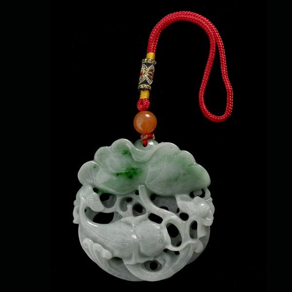 CARVED JADE PENDANT.: CARVED JADE PENDANT. Designed featuring a lotus flower, fish and coins, all intertwined from a carved and pierced jadeite plaque measuring approximately 54.00mm x 11.00mm, suspending from a strung jad
