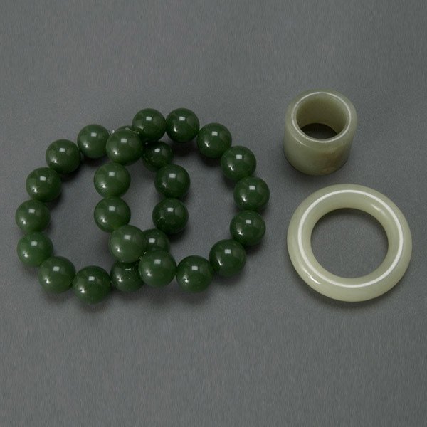 Four Chinese Jades and Spinach Jades, 19th/20th C: Four Chinese Jades and Spinach Jades, 19th/20th Century. Two bracelets of large dark green beads; one archer ring of deep celadon hue and slight caramel inclusions; one pale green ring. {Diameter of f