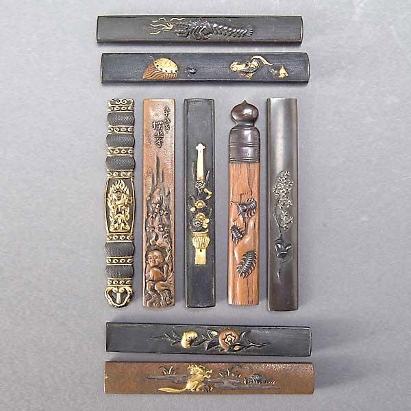 Nine Shakudo or Bronze Kozukas: Nine Shakudo or Bronze Kozukas, with Buddhist or flora/fauna subject, three signed verso {Height 3 3/4 inches}