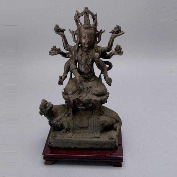 A Cast Iron Figure of an Eight-Armed Buddhist Deit: A Cast Iron Figure of an Eight-Armed Buddhist Deity, each hand holding a different auspicious object, cast with an ornately jeweled necklace and Buddha headdress, seated upon a lotus pedestal supporte