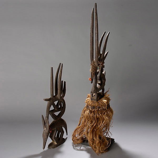 Two Bambara chi wara: Two BAMBARA antelope headdresses, chi wara (tji wara). Blackened wood with fiber tassels, beads, shells, raffia. Height of female 34 3/4 inches. In good condition, tip of horn on female missing.