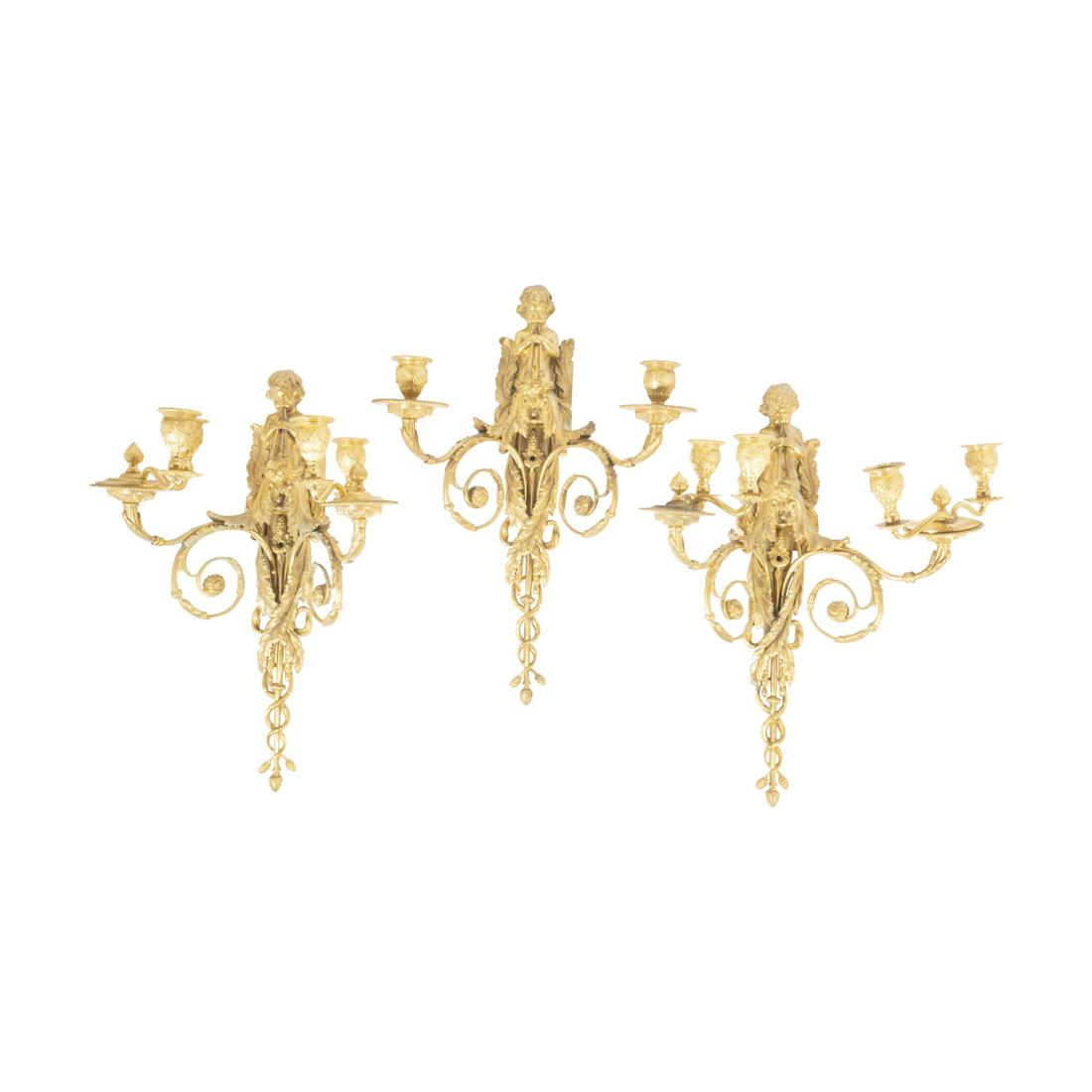 Three Ormolu Sconces: Three Ormolu Sconces. Figural, cherubic trumpet players; one with two lights, the others with four lights. {Approximate dimensions: 17 1/4 inches high.}. Condition: Break to one bottom portion. Appare