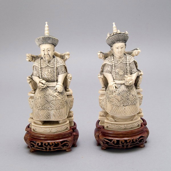 A Pair of Seated Ivory Figures of Emperor & Empres: A Pair of Seated Ivory Figures of Emperor and Empress, each holding either a fruit form or scepter, shown wearing elaborately designed robes and hats, seated upon either a carved dragon or phoenix arm
